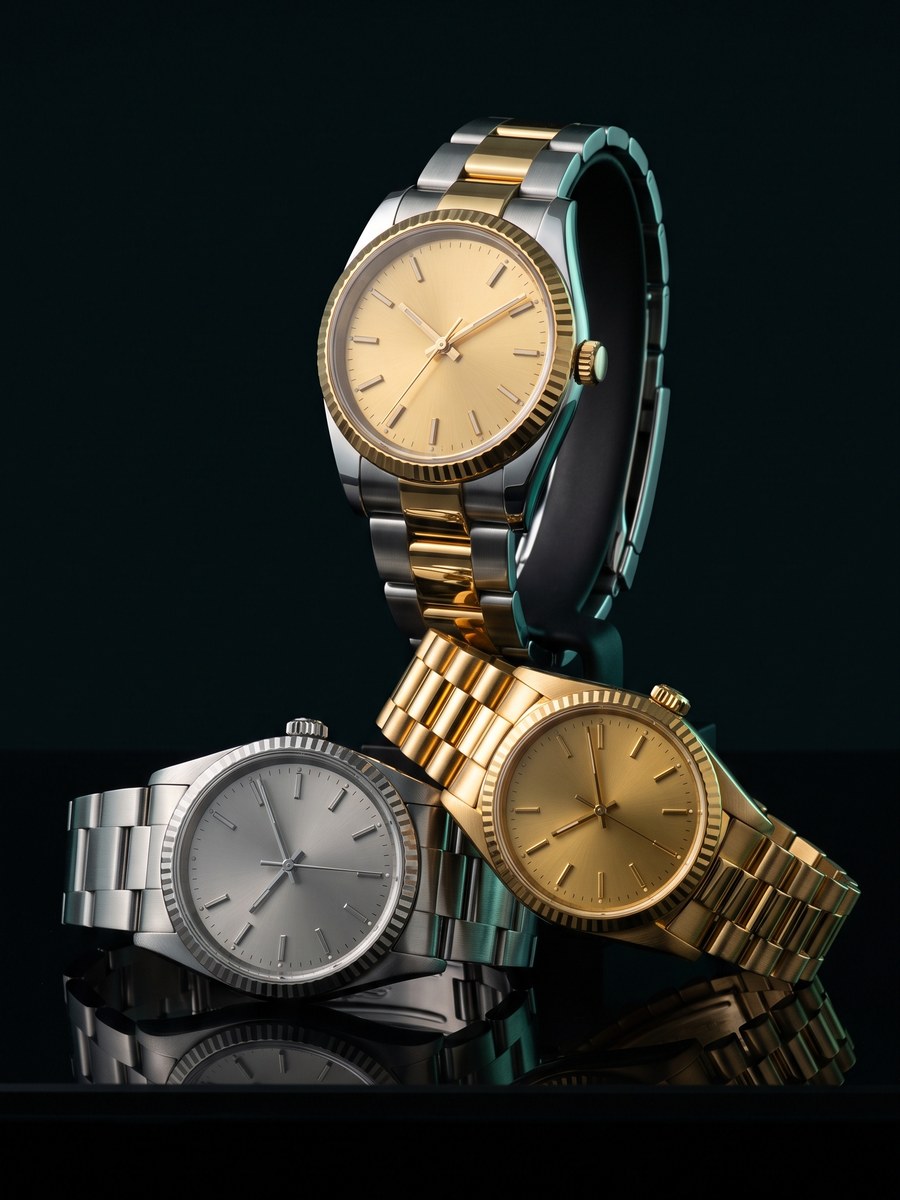 Three wristwatches on black glass — two-tone steel and gold, all-steel, and yellow gold.